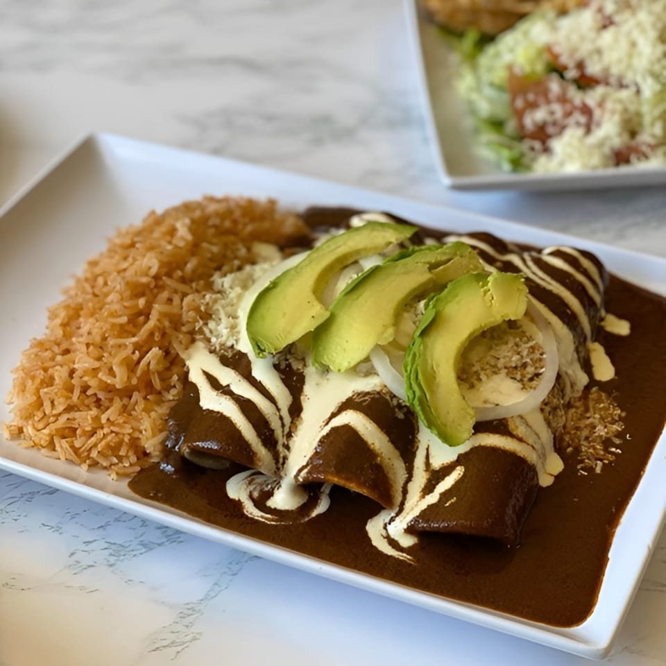 Enchiladas with mole sauce, sour cream, avocado, onions, and rice on a white rectangular plate.