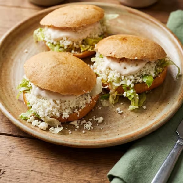 Three gorditas filled with lettuce, crumbled white cheese, and cream on a rustic plate.