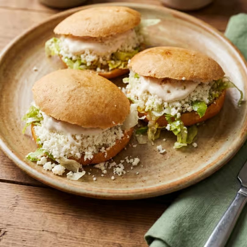 Three gorditas filled with lettuce, crumbled white cheese, and cream on a rustic plate.