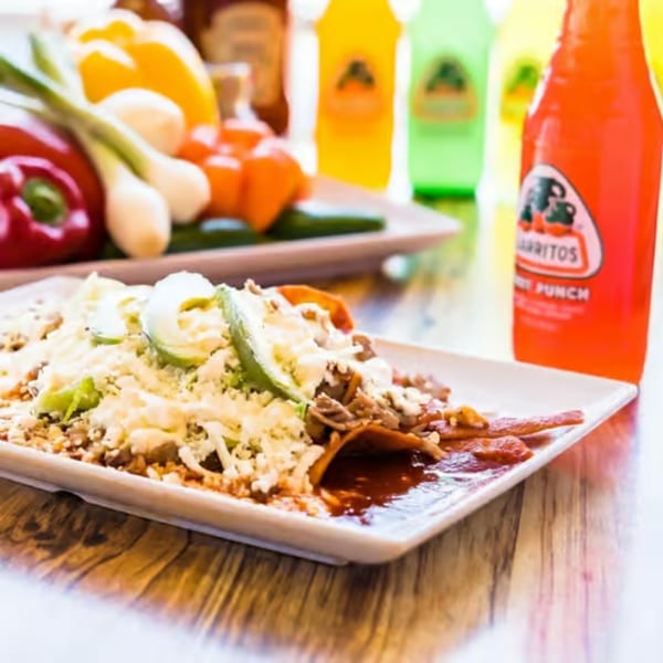 A plate of chilaquiles with cheese and avocado, fresh vegetables, and Jarritos sodas.