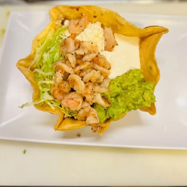 Shrimp taco salad in a crispy tortilla bowl with lettuce, cheese, sour cream, and guacamole.