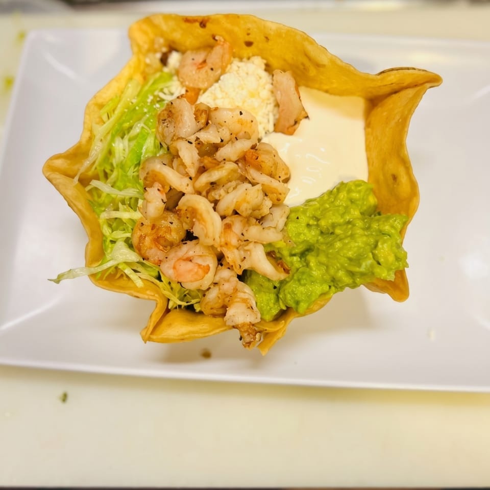 Shrimp taco salad in a crispy tortilla bowl with lettuce, cheese, sour cream, and guacamole.